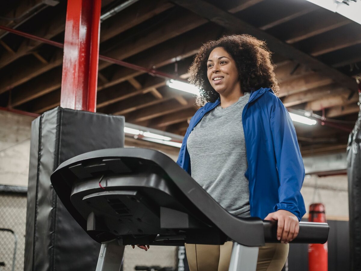 A woman smiling while walking on a treadmill in a gym.