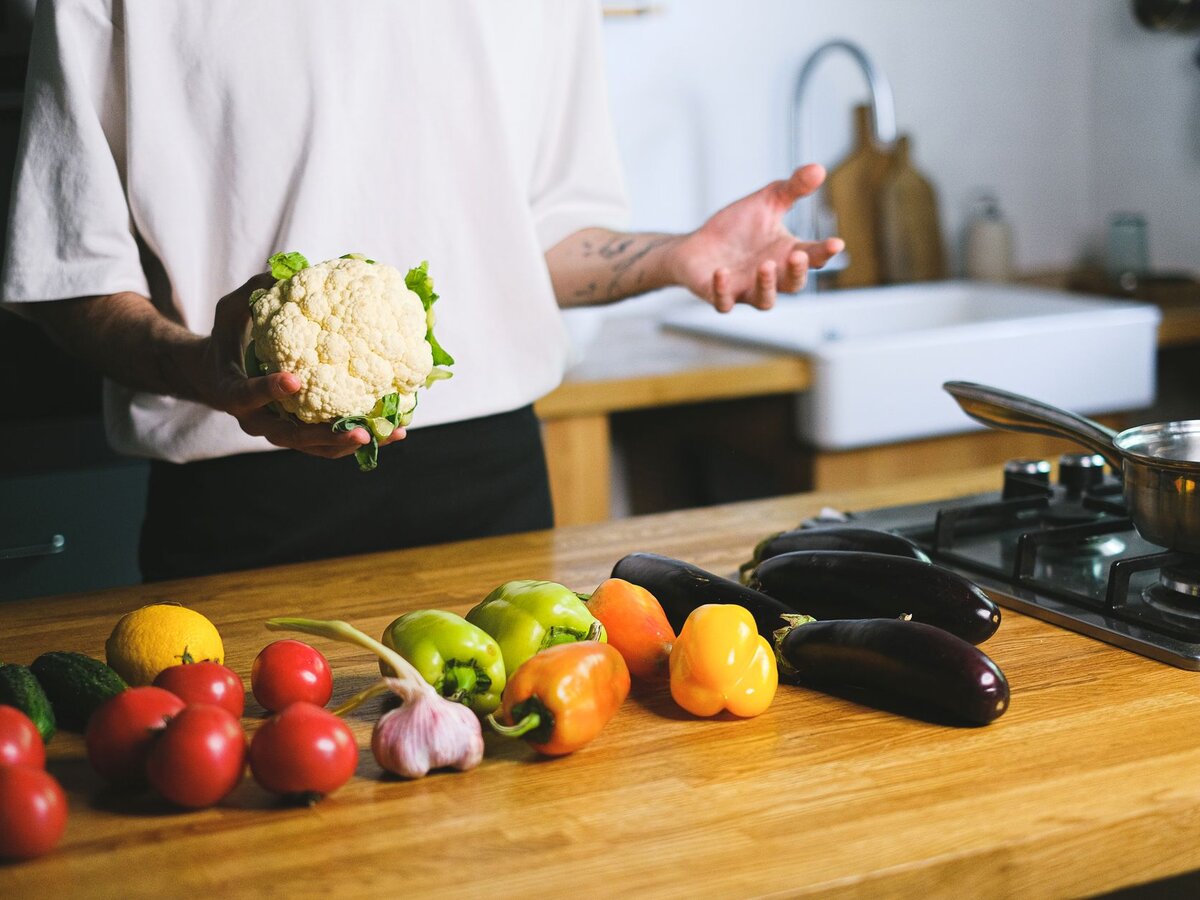 A person standing by a kitchen counter with fresh vegetables laid out.