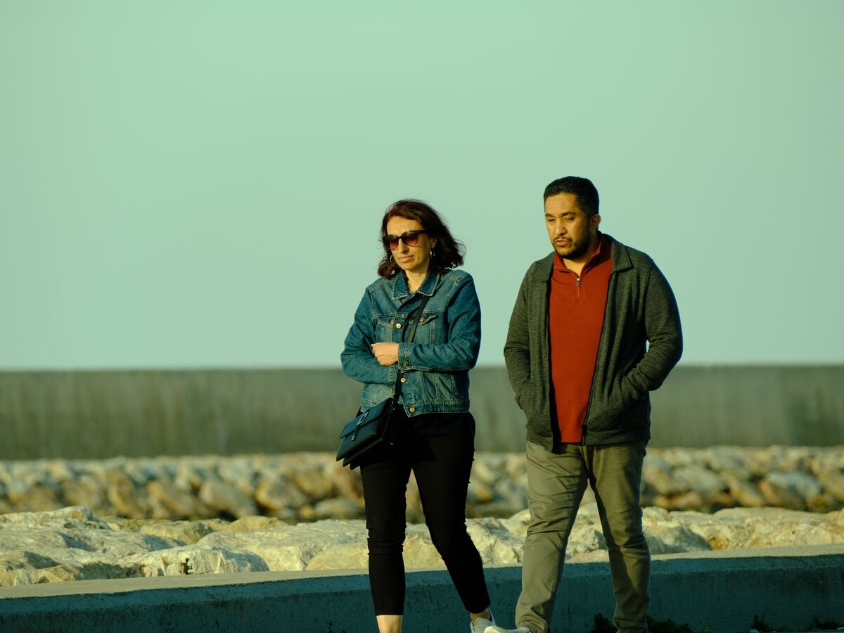 A man and woman walking together along a paved waterfront promenade during golden hour.